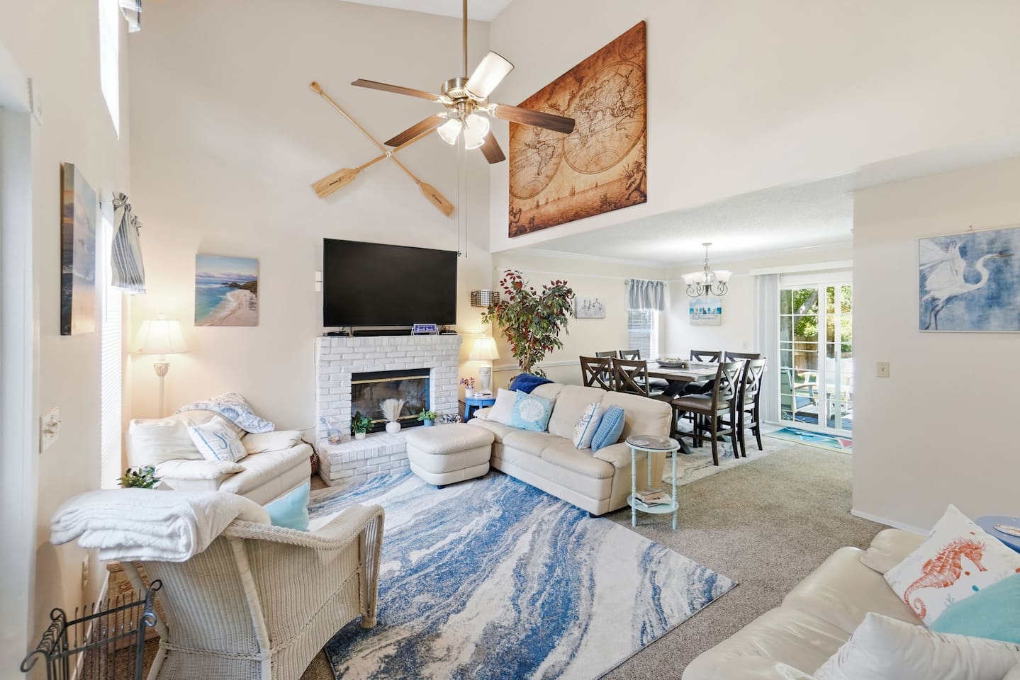 Bright, open living room with vaulted ceilings, fireplace, large TV, and adjoining dining space.