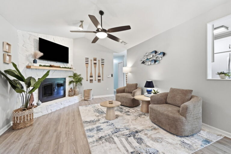 A bright coastal-inspired living room with comfortable seating, a large TV, and a statement fireplac